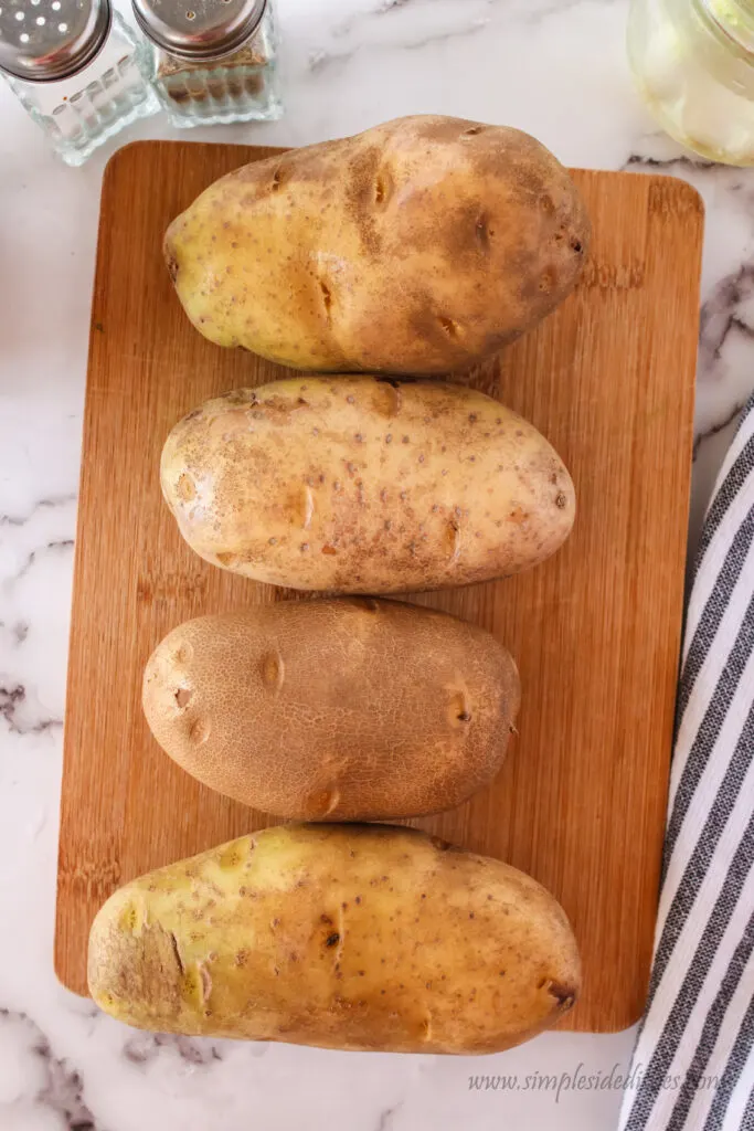 4 russet potatoes lined up on a cutting board.