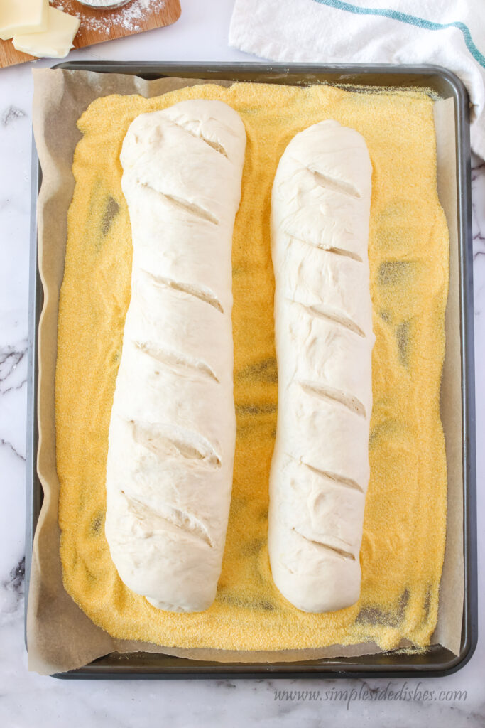 cookie sheet covered in cornmeal with two loaves of french bread