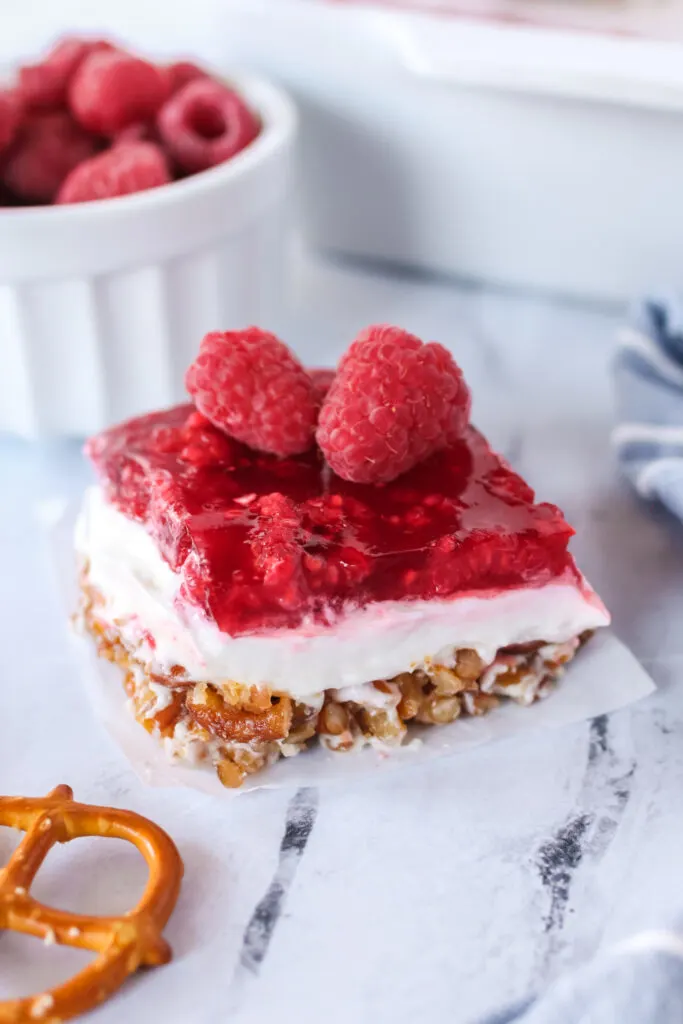 Raspberry Pretzel Salad sliced and put on a plate with 2 fresh raspberries on top.