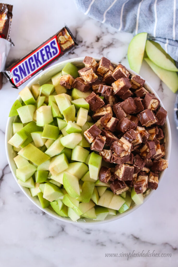 snickers and apples in a bowl on top of pudding mixture.