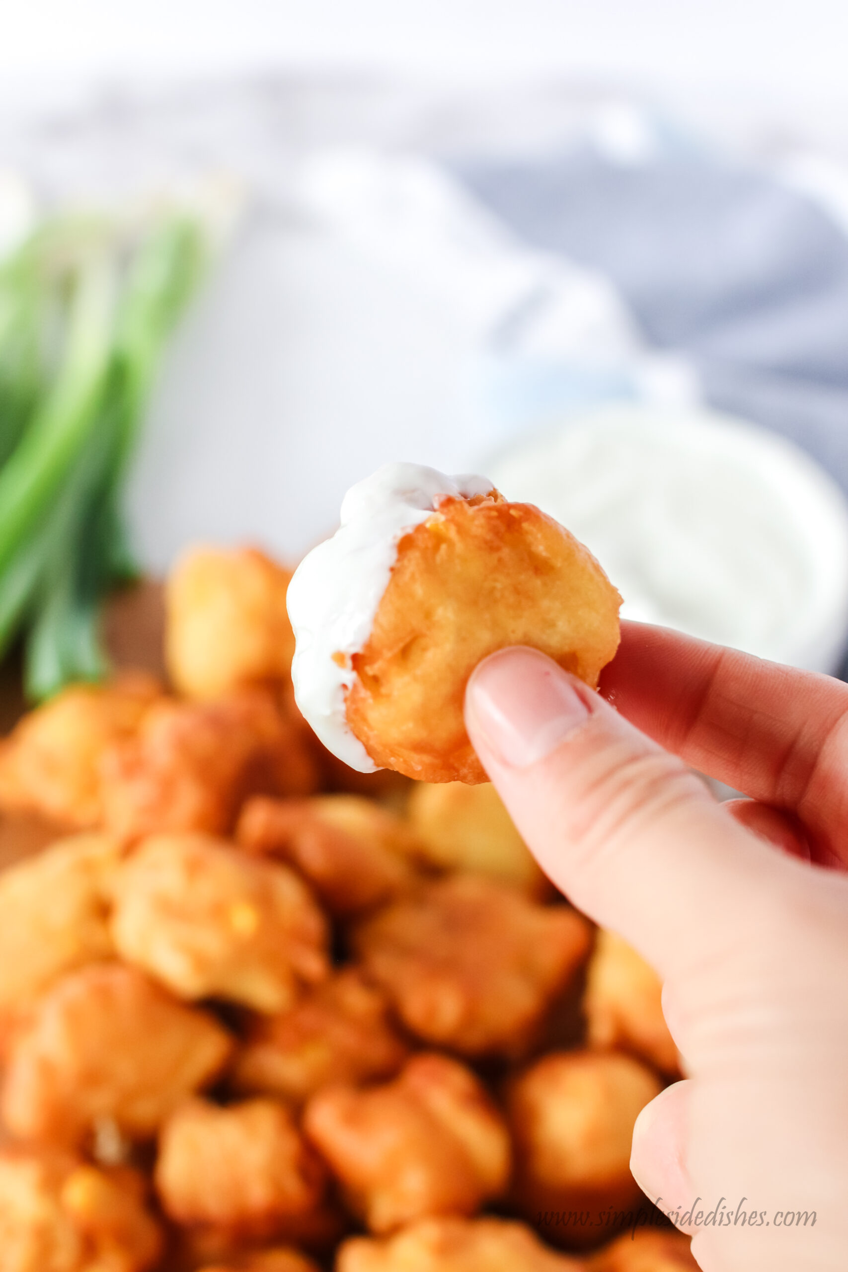 hand holding fritter with sour cream dip