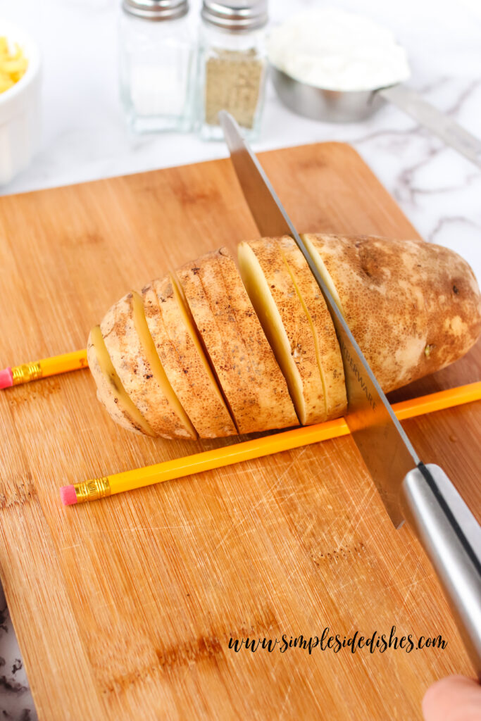 potato surrounded by two pencils and a knife slicing slits into it