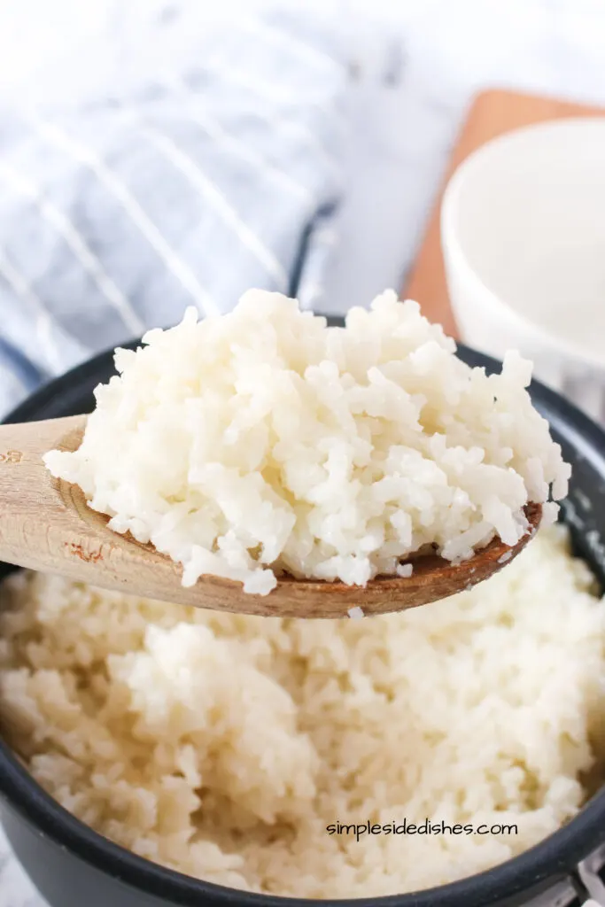 wooden spoon full of rice held above pot of cooked rice.