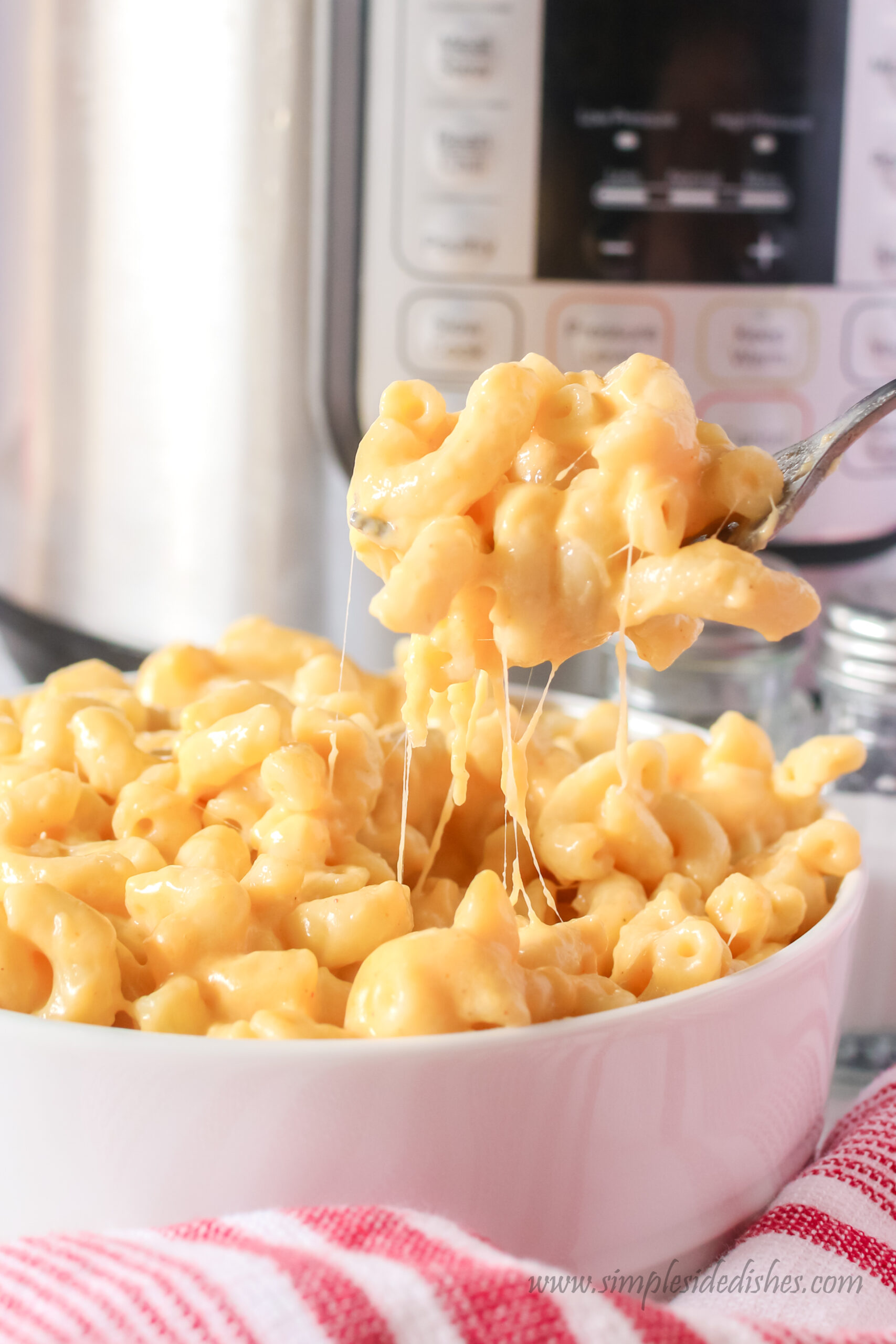 bowl of macaroni with a fork being held above bowl, with a cheese pull happening between bowl and fork.