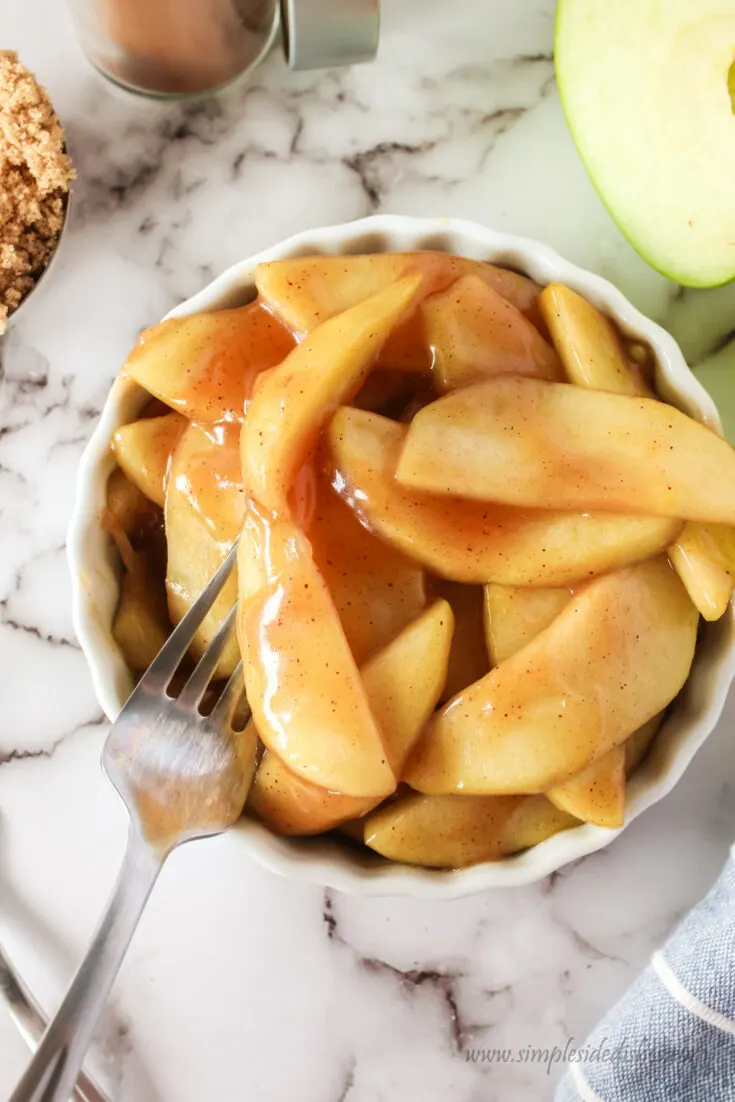 fried apples in dish with a fork pricking one.
