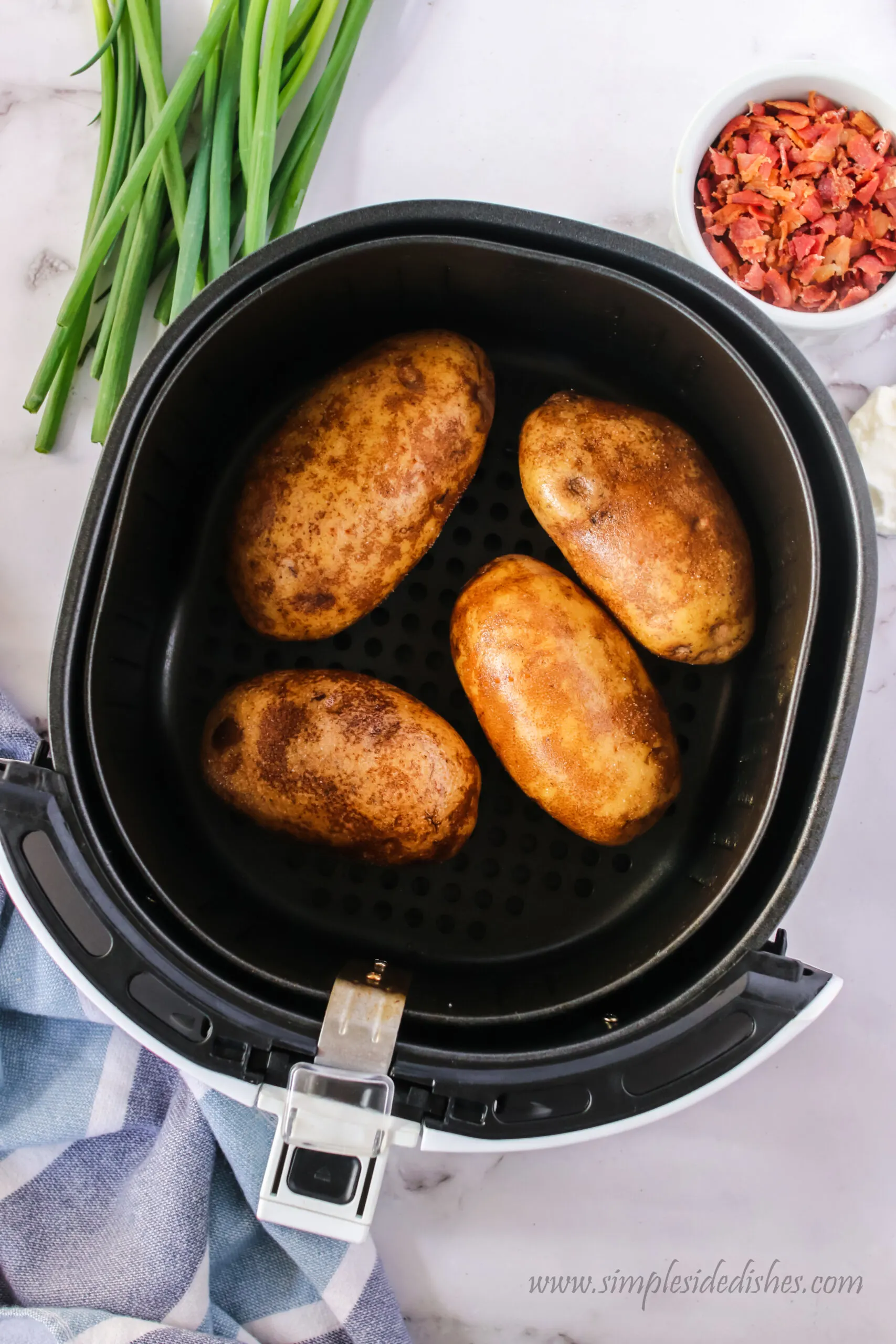 4 potatoes placed into air fryer basket, ready to cook