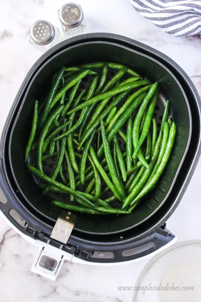 fresh green beans placed in an air fryer, uncooked.