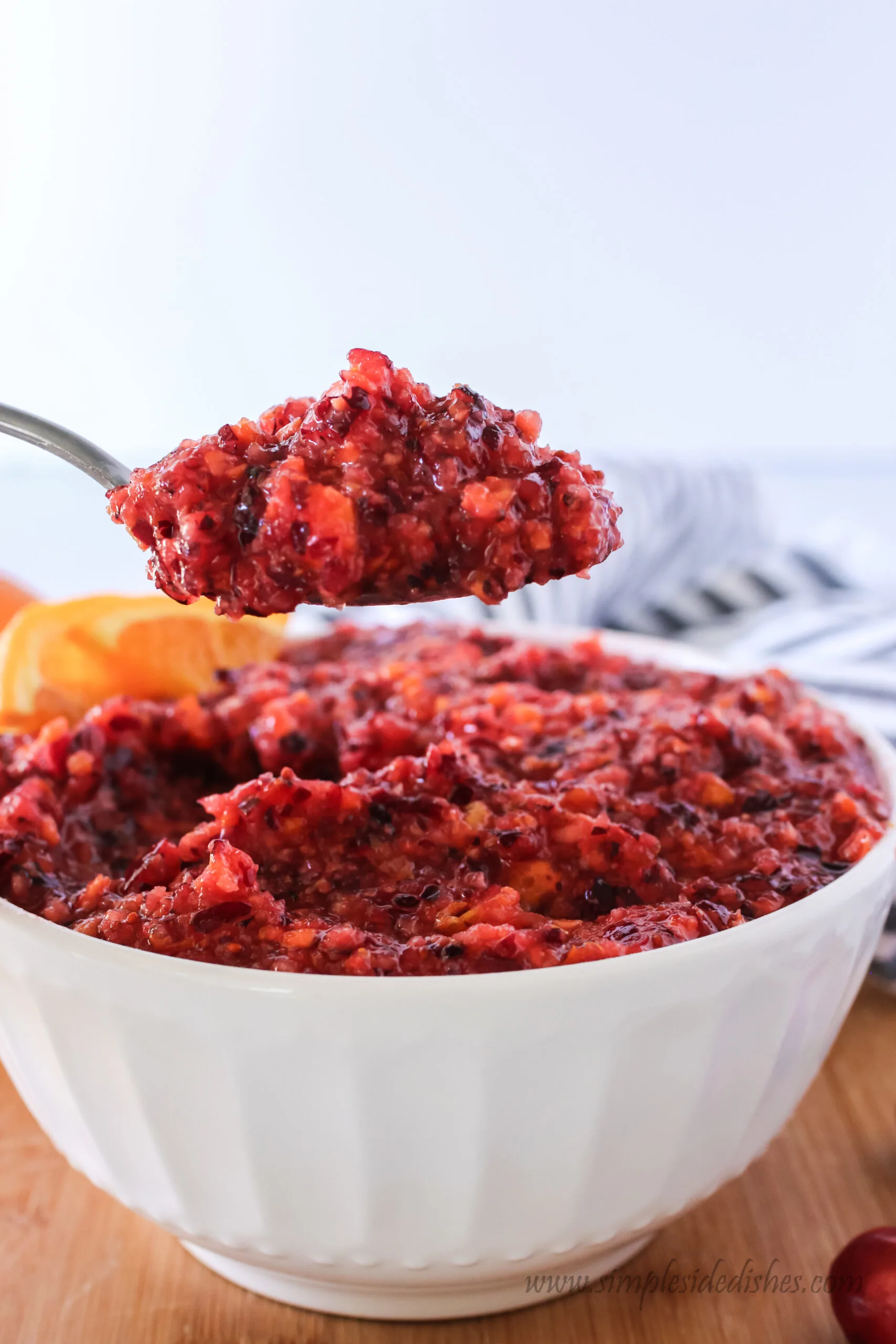bowl of cranberry relish with a spoon being held above full of relish.