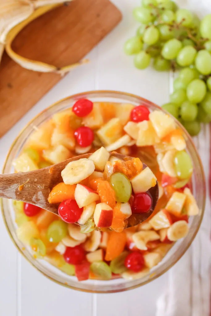 top looking down at fruit salad in bowl with a wooden spoon scooping a portion out