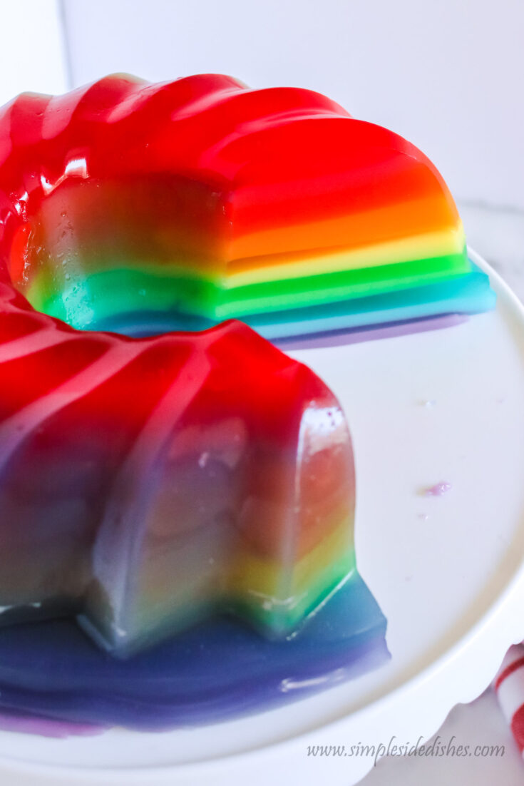 zoomed out image of rainbow jello on platter with a slice cut out