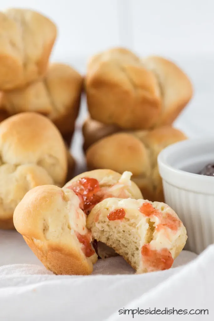 rolls stacked in background. One roll up front with butter and jam and a bite removed