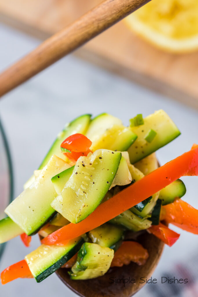 wooden spoon scooping out a portion of zucchini and bell pepper side dish.