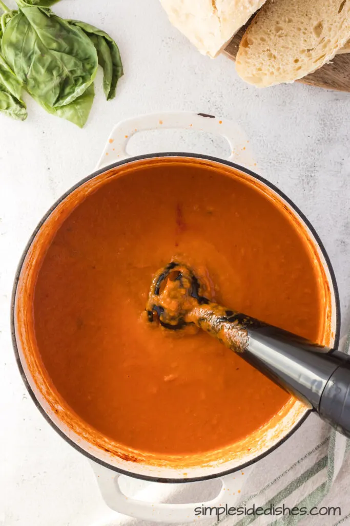 A small hand blender in pot, blending vegetables to create a creamy soup