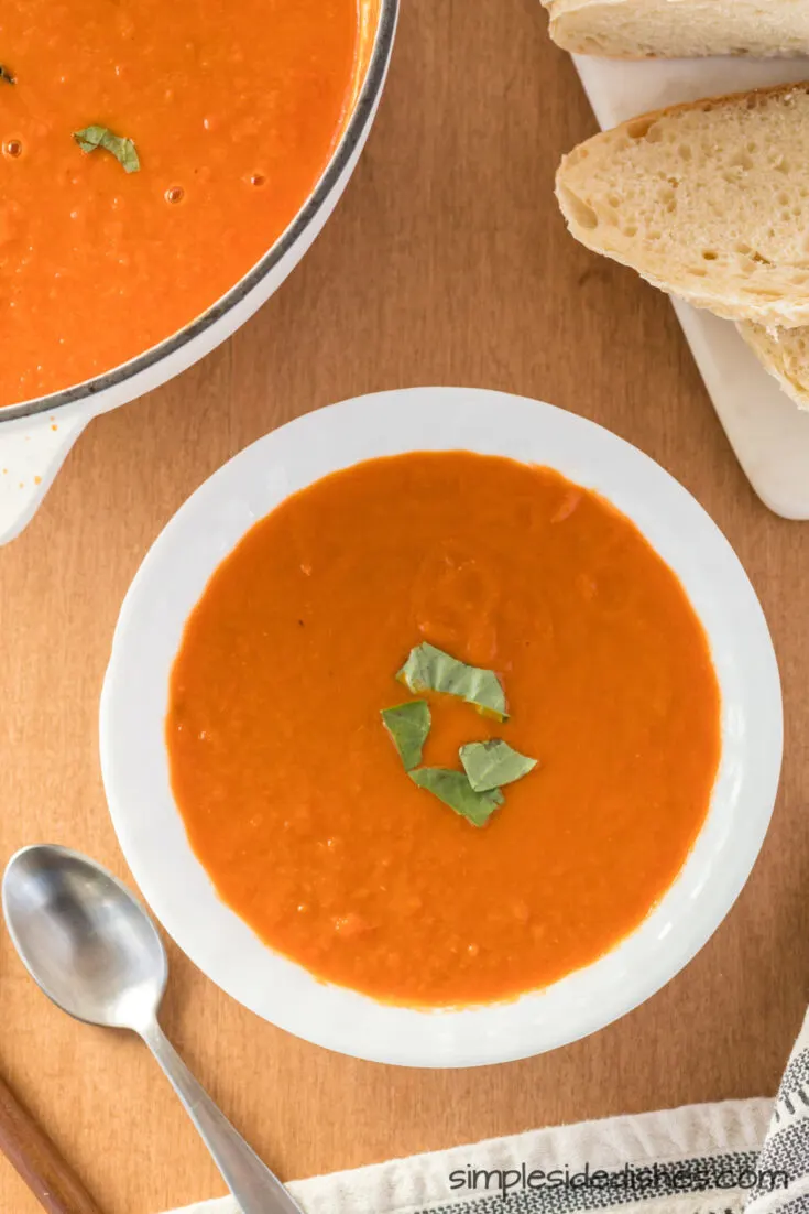 zoomed out image of tomato soup in a bowl with pot of soup behind.