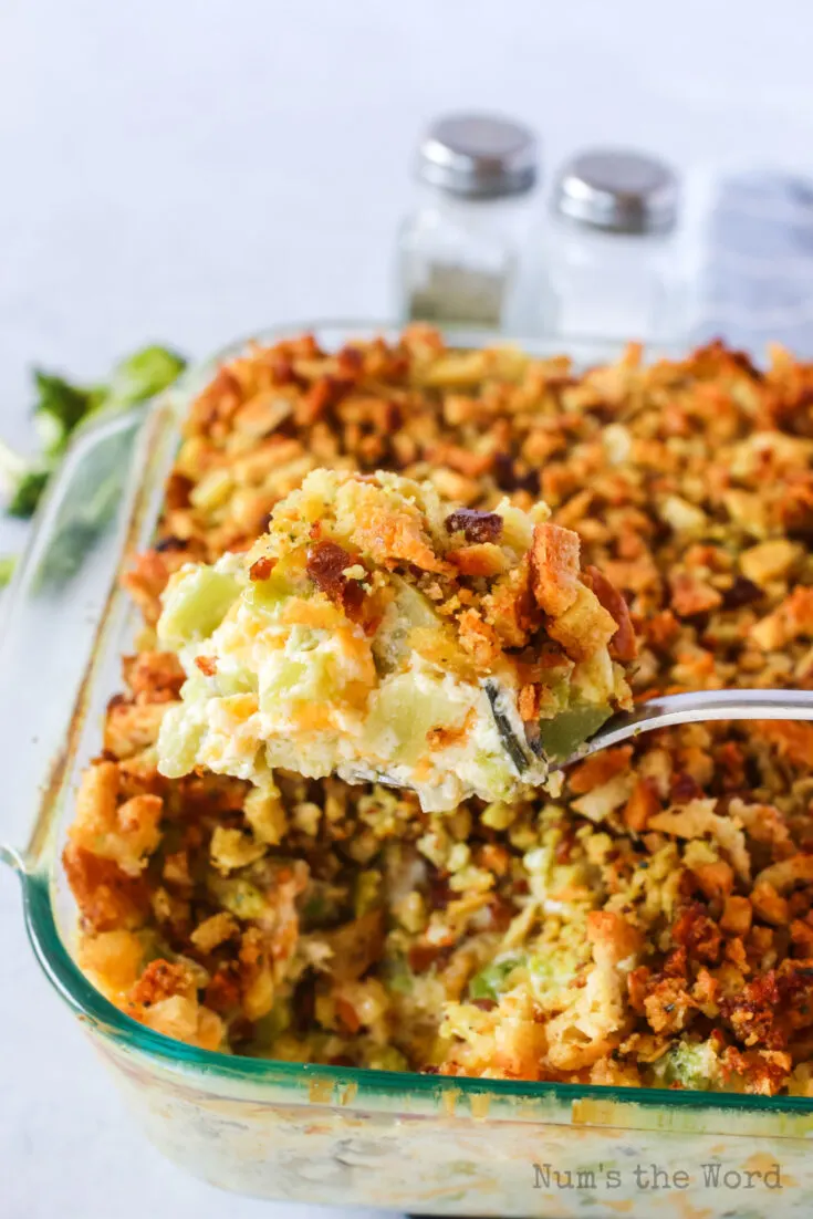 Baked Cheesy Broccoli Stuffing Casserole in pan with a spoon scooping a portion out.