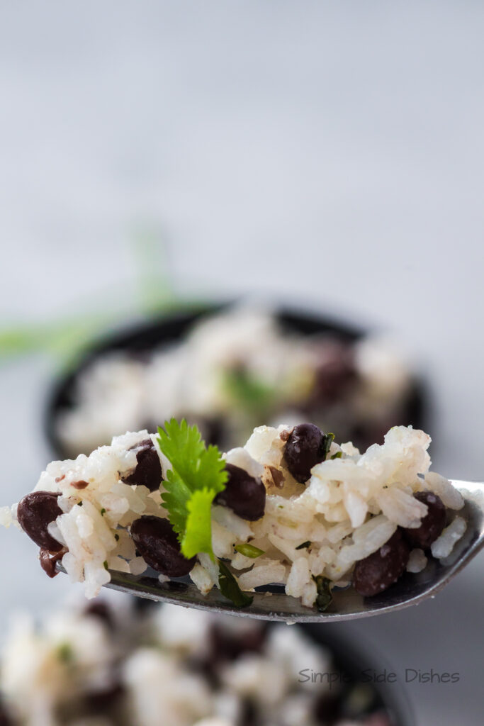 a spoon full of black beans and rice being held above a bowl.