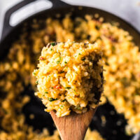wooden spoon scooping a portion of cauliflower rice out of the skillet