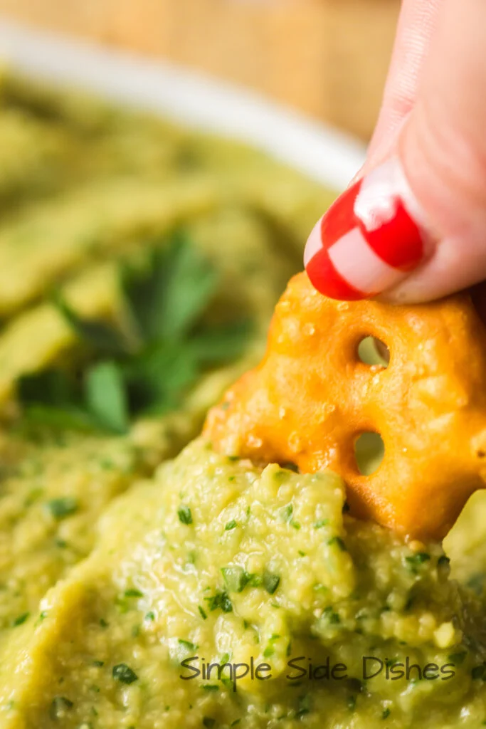 Hand holding a pretzel and dipping it into the hummus.