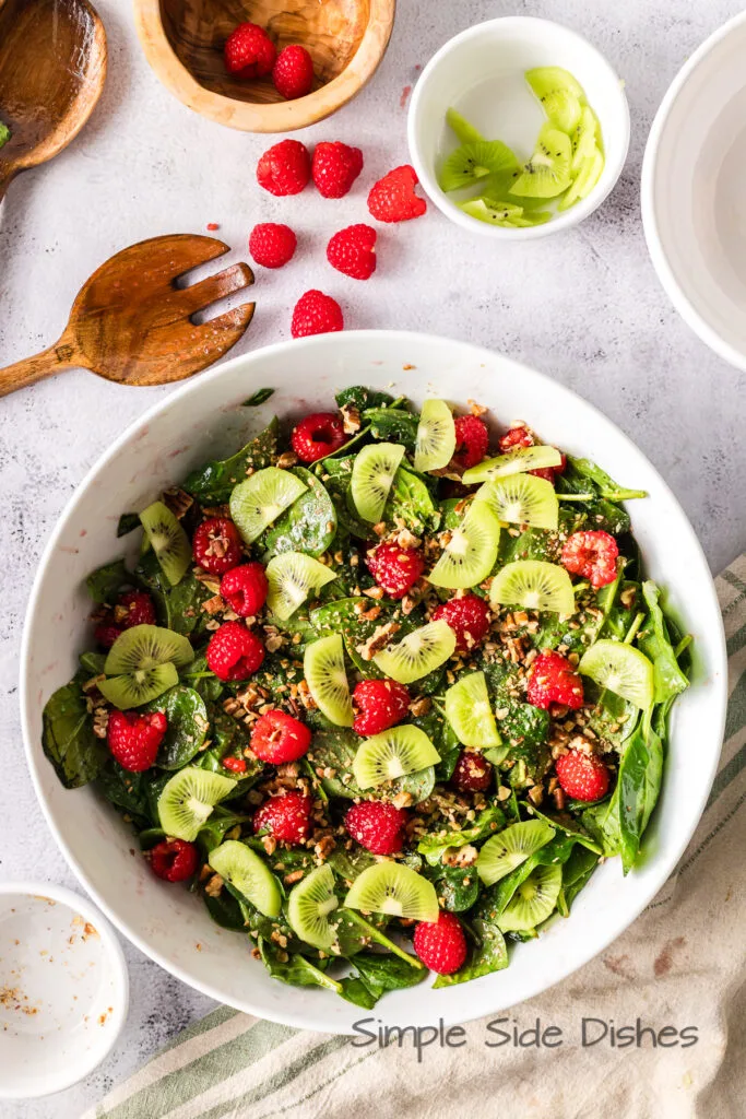 sliced kiwis placed on top of raspberries, spinach and pecans.