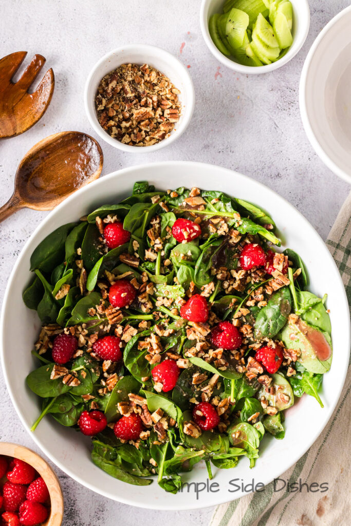 pecans scattered on top of raspberries and spinach.