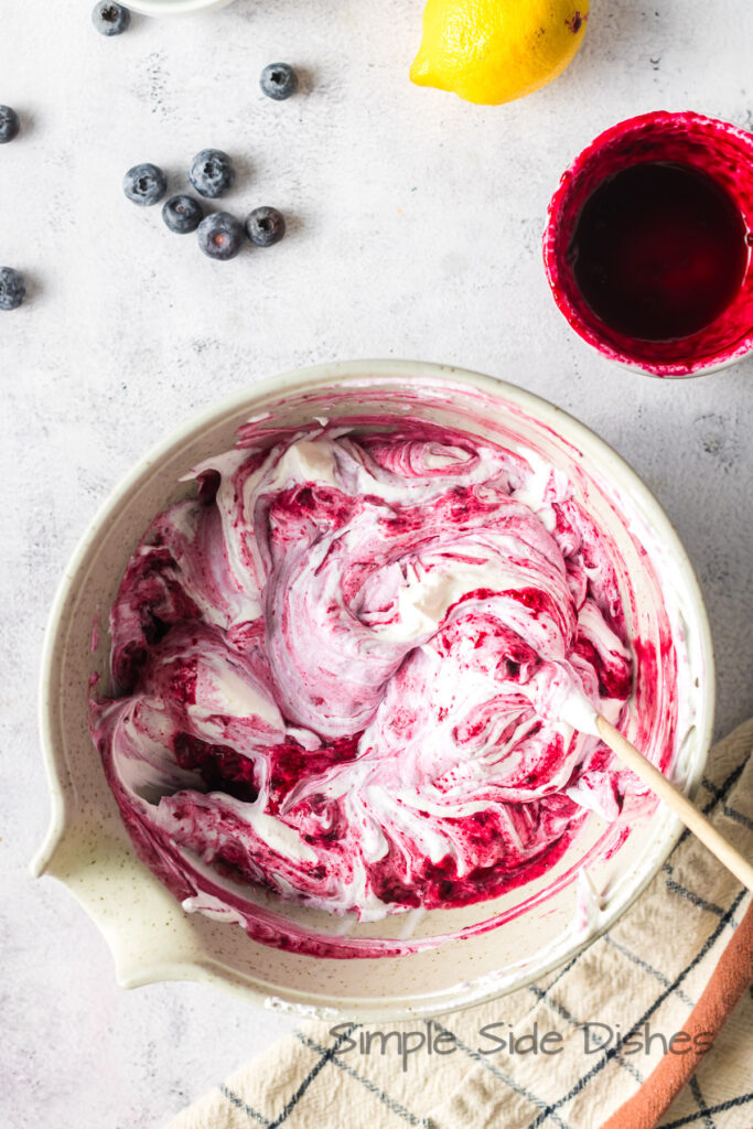 A spatula swirling whipped cream and blueberry mixture.