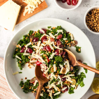 Prepared kale salad in a serving bowl with wooden tongs