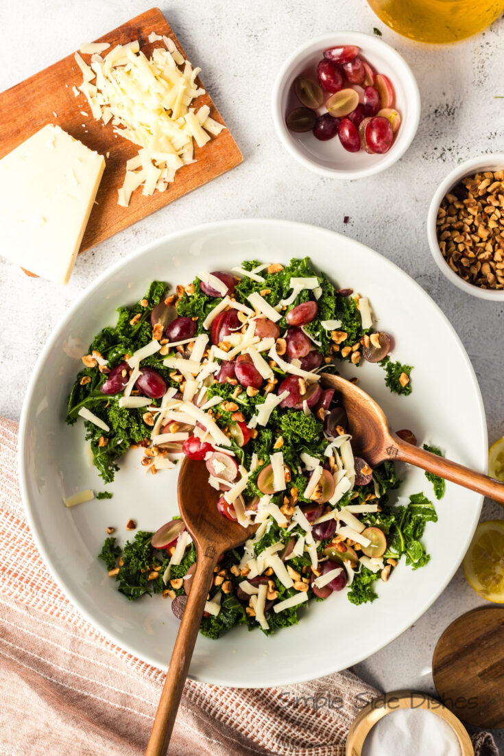 Prepared kale salad in a serving bowl with wooden tongs